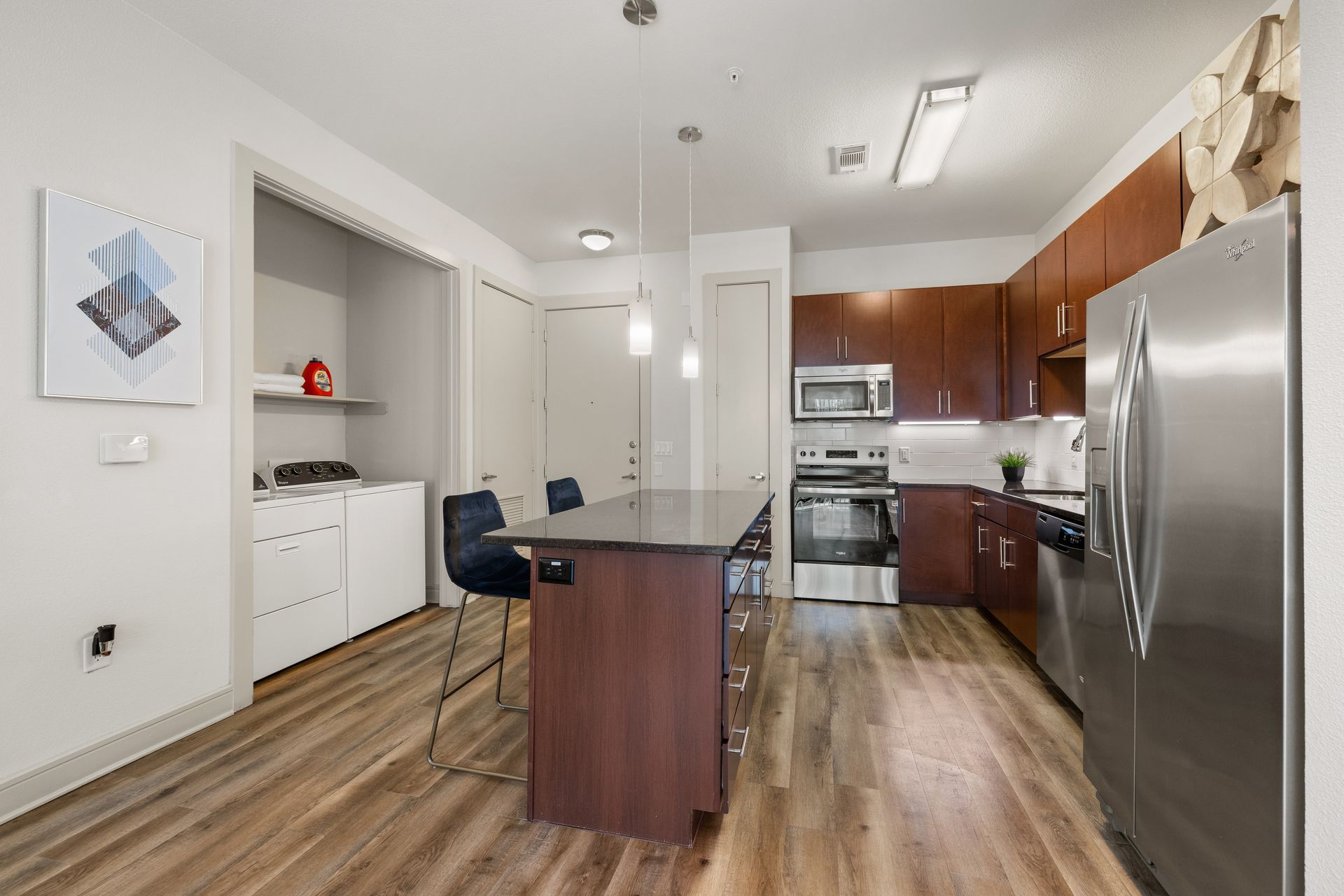 Modern kitchen with island, stainless steel fridge, white cabinets, and wood flooring at Sabina in Austin, TX.