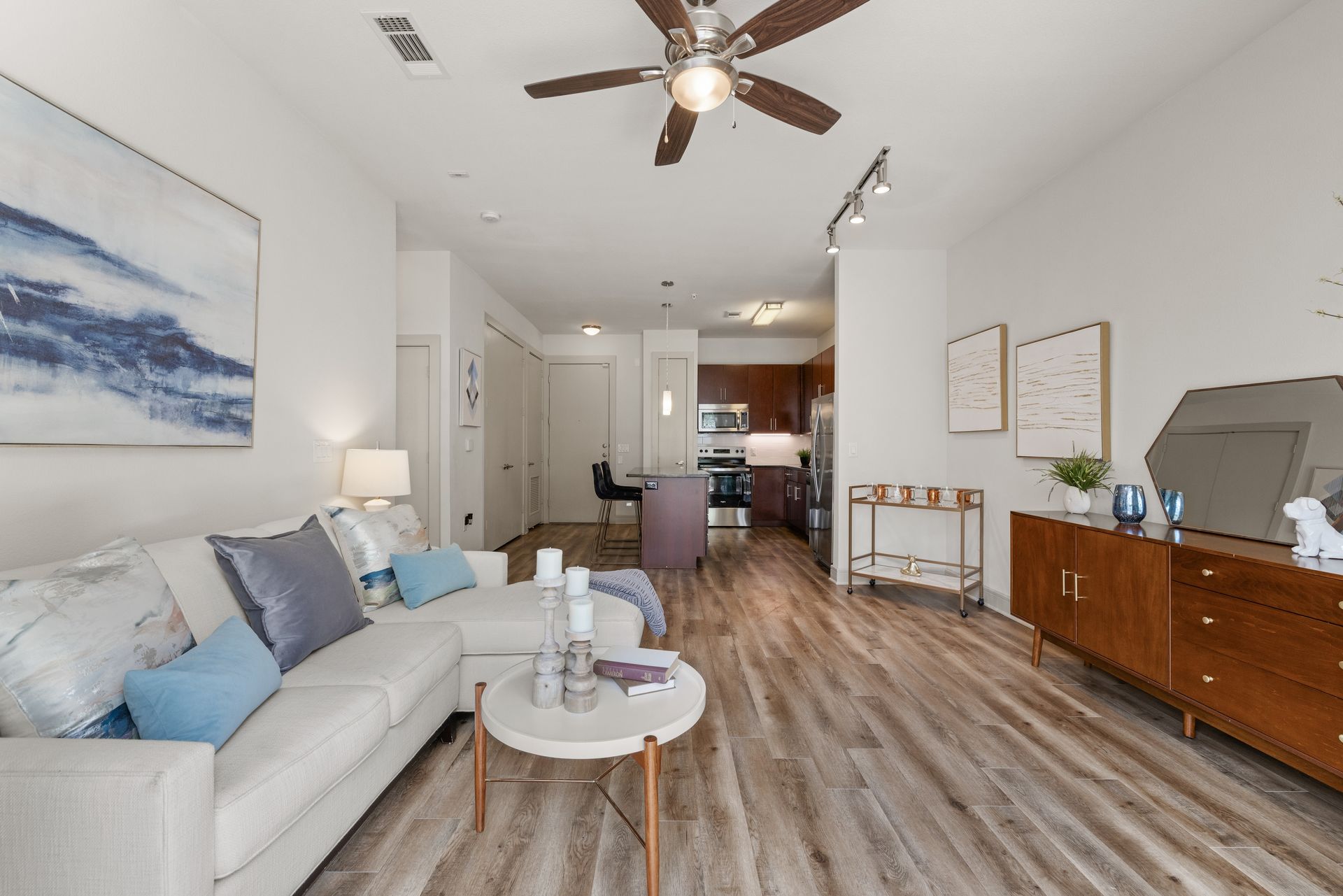 Modern living room with white sofa, wood floor, ceiling fan, and TV console at Sabina in Austin, TX.