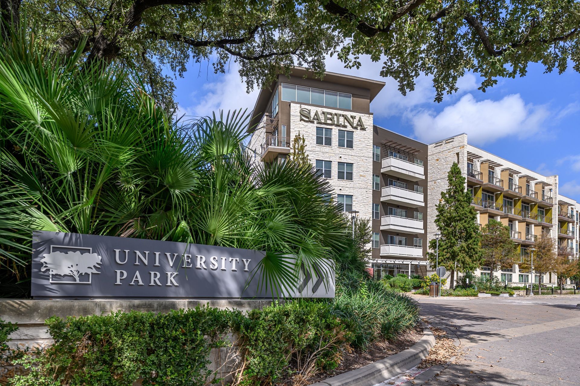 University Park apartment building entrance sign; lush greenery, blue sky.