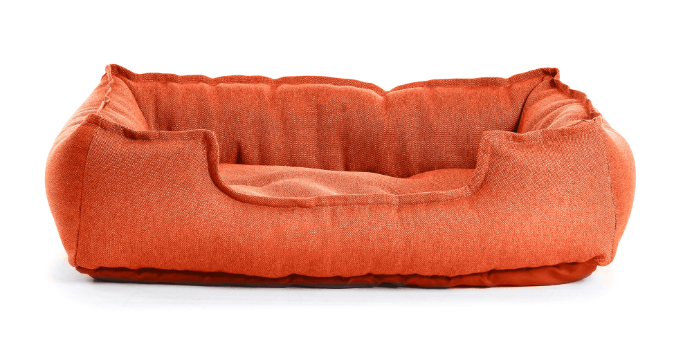 An orange dog bed is sitting on a white surface.