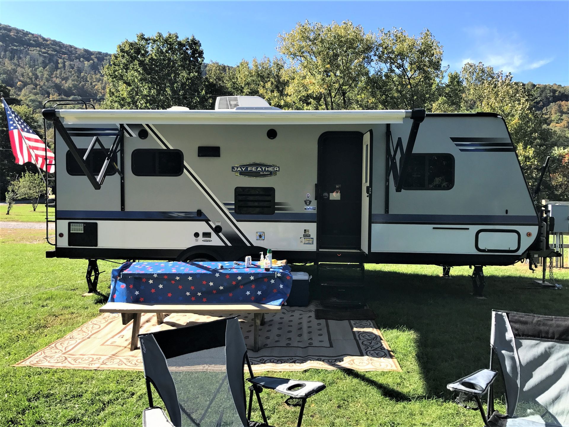 RV parked on grass with table, chairs, and American flag.