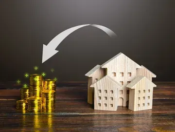 Stacks of gold coins being invested into wooden houses; down arrow depicts money transfer.