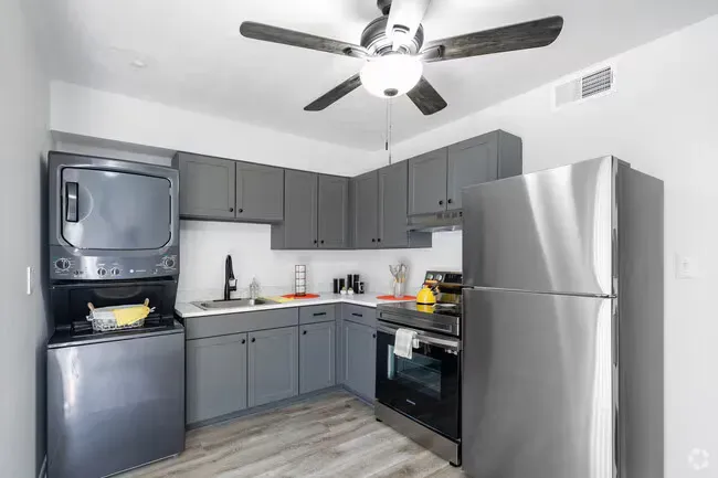 Small, modern kitchen with gray cabinets, stainless steel appliances, and a stacked washer/dryer.