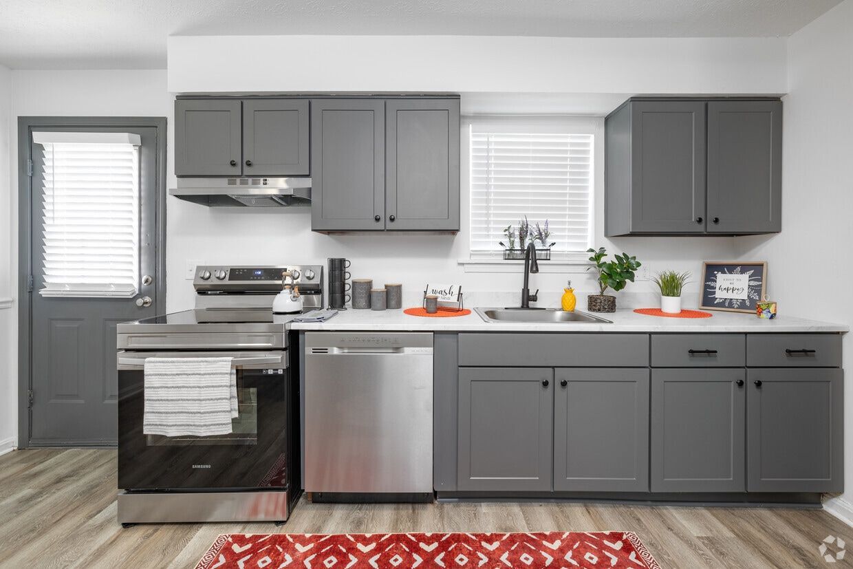 Gray kitchen with stainless steel appliances and cabinets, white countertops, and a red rug.