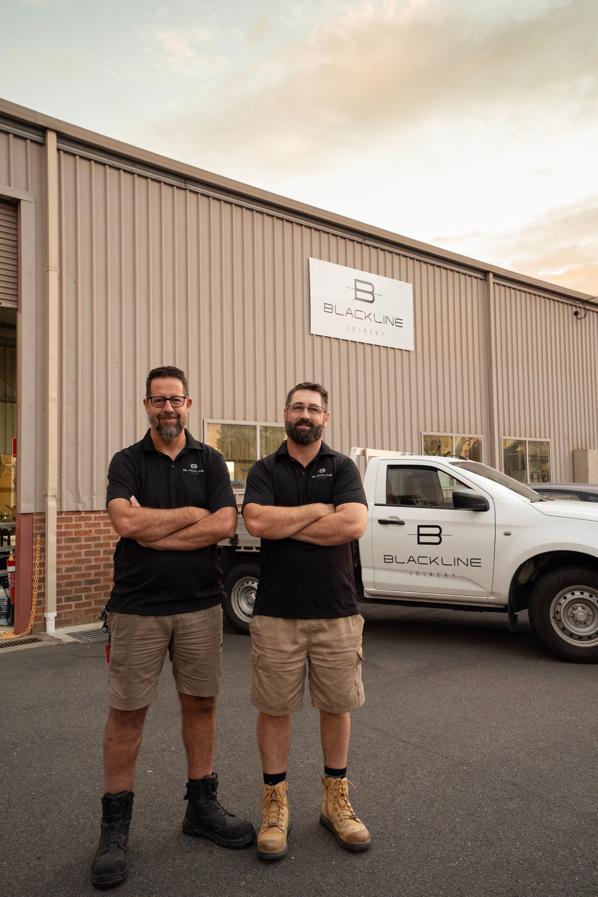 Two people standing in a manufacturing workshop next to a large industrial CNC machine with a vacuum hose attached.