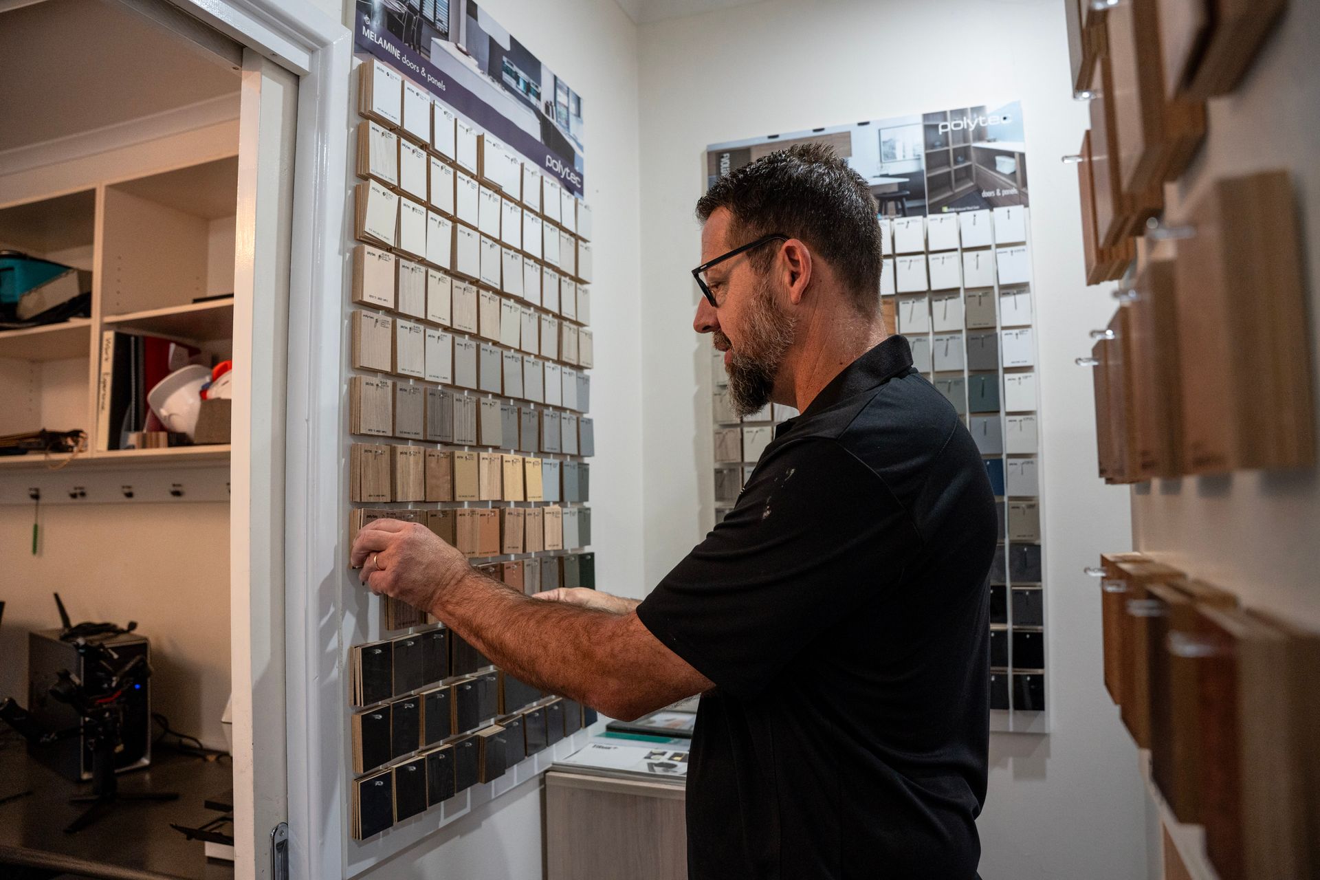 A person with glasses examines a wall display of various paint or material samples in a design or hardware store.