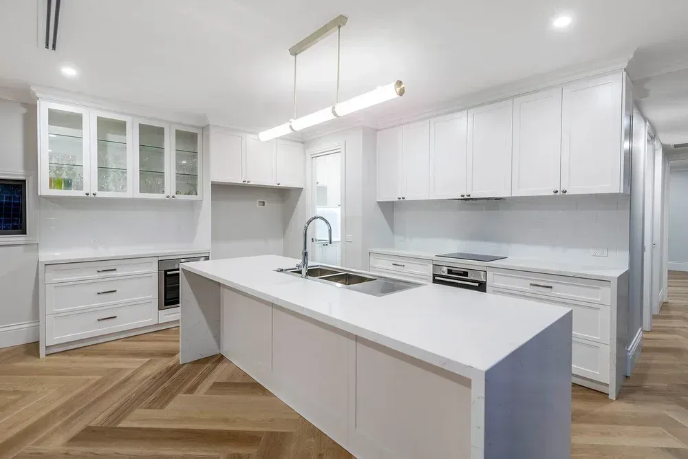 Modern white kitchen with island, herringbone wood floor, and built-in cabinets