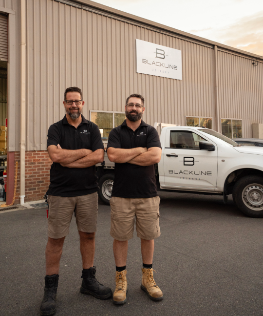 Two men in black polos stand outside a Black Inc building beside a branded white pickup truck.