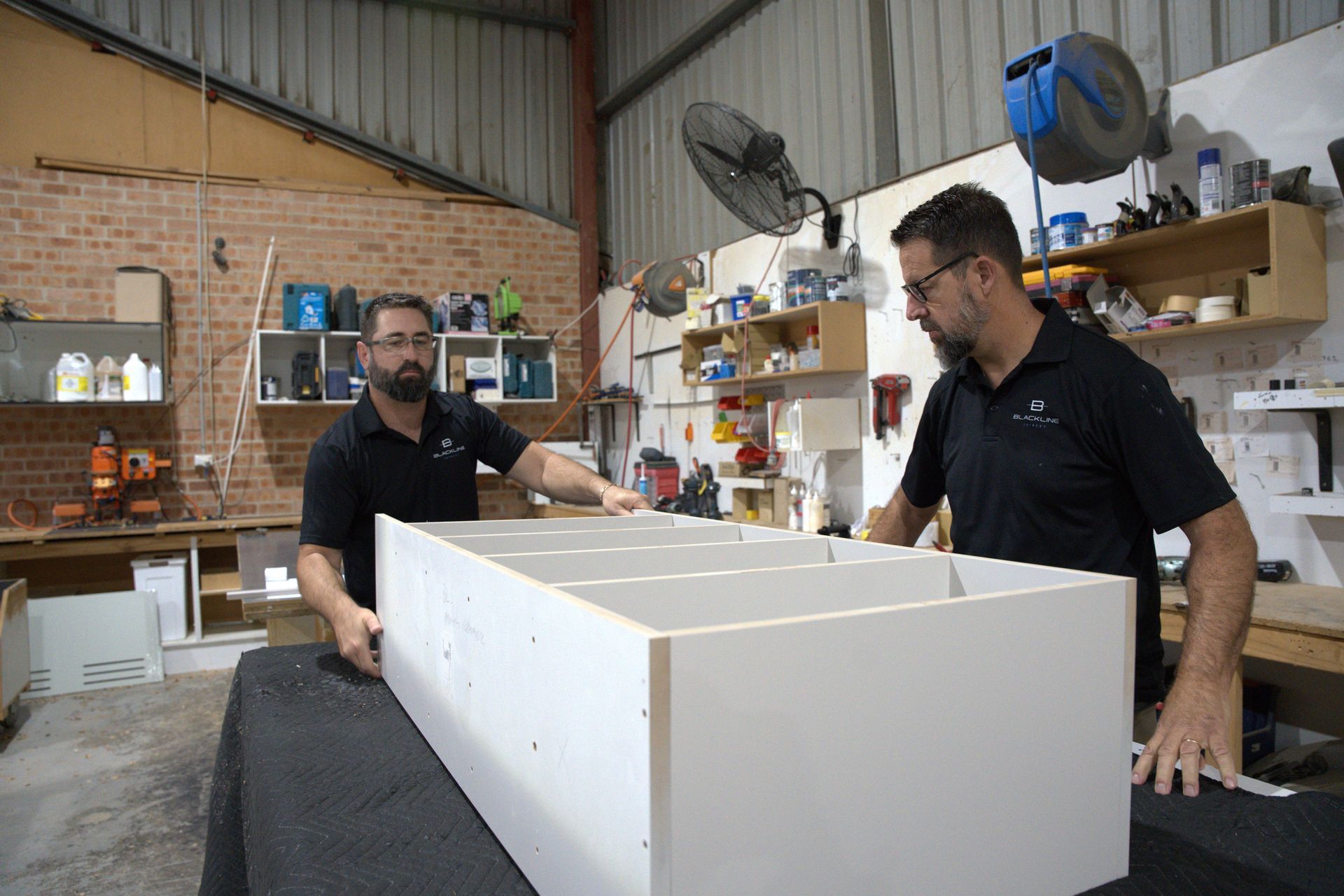 A home office nook with navy blue cabinets, a white desk, and a cushioned L-shaped bench seat against a neutral wall.