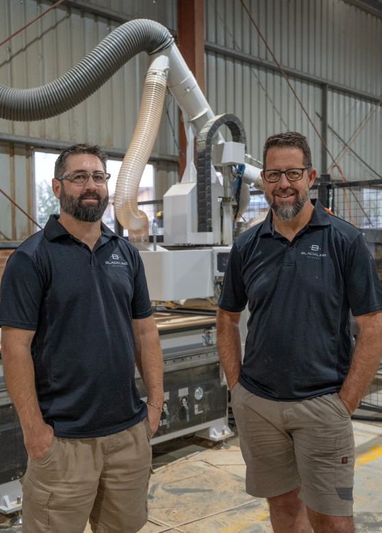 Two men in black polos stand beside a large industrial machine in a workshop.