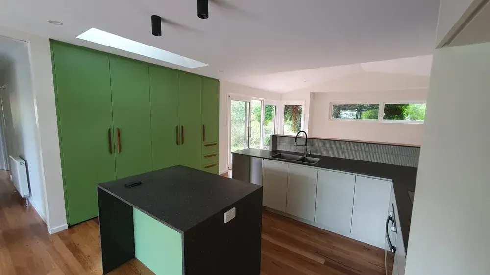 Modern kitchen with green cabinets, black island, white walls, wood floors, and windows letting in daylight
