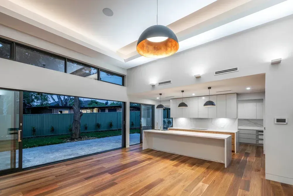 Modern open-plan kitchen with white island, wood floors, and large sliding glass doors to a patio