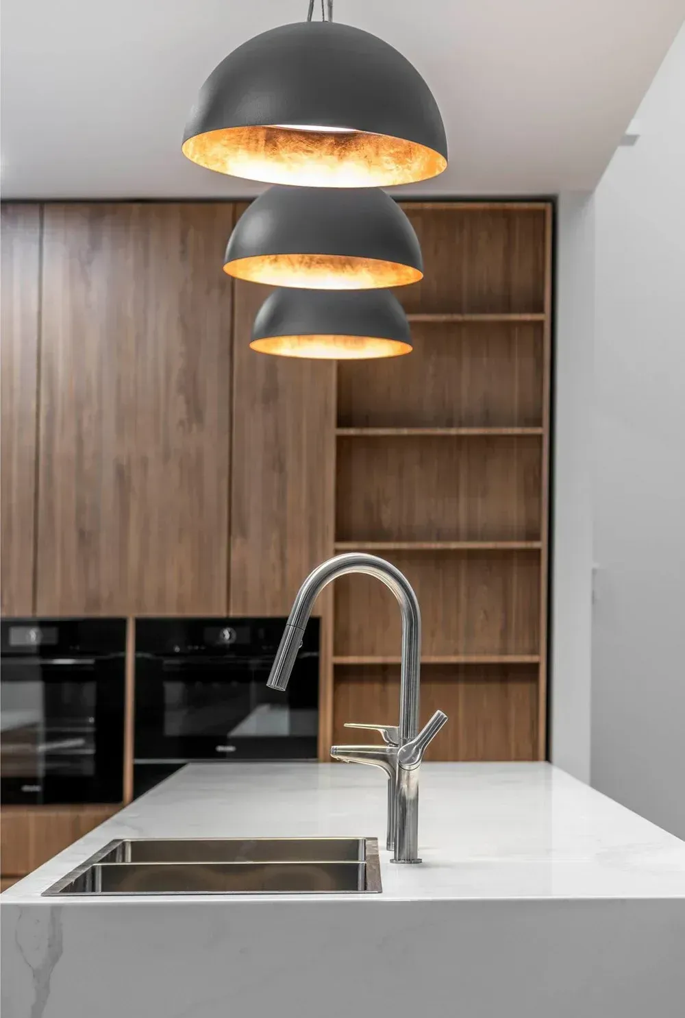 Modern kitchen with white island, stainless sink, wood cabinets, and three black pendant lights.
