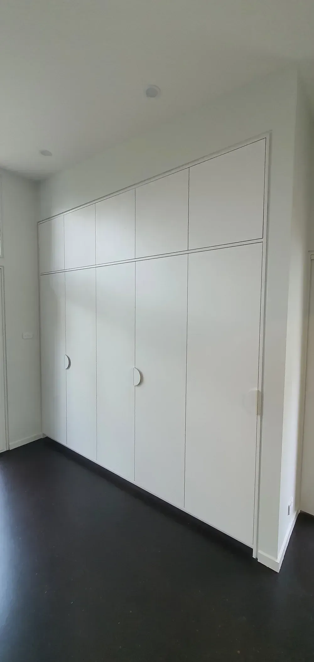 White wall of built-in cabinets with handles in a bright room, black floor and white ceiling
