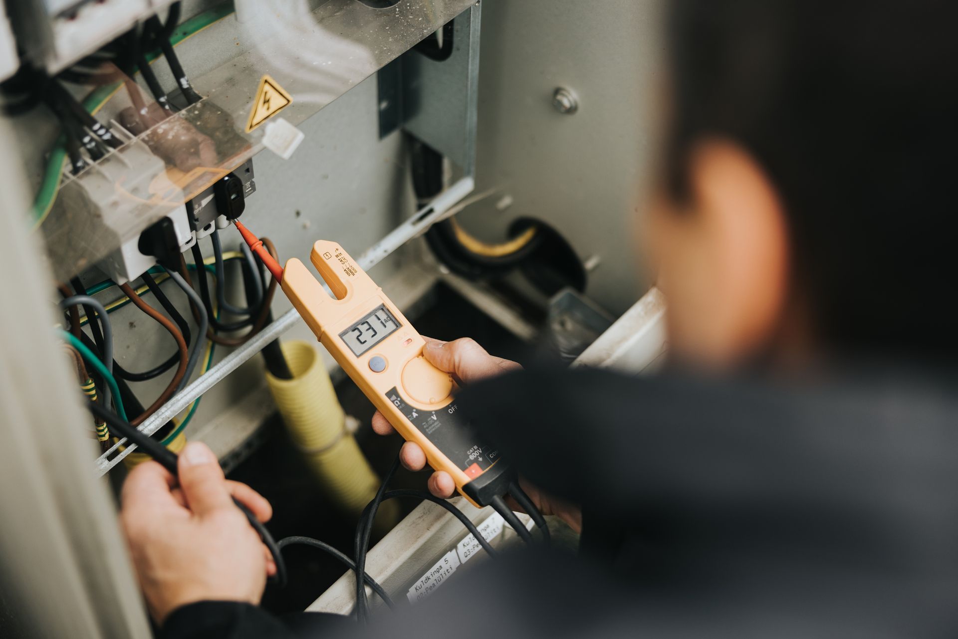 Technician using a multimeter to test electrical wiring in a panel.