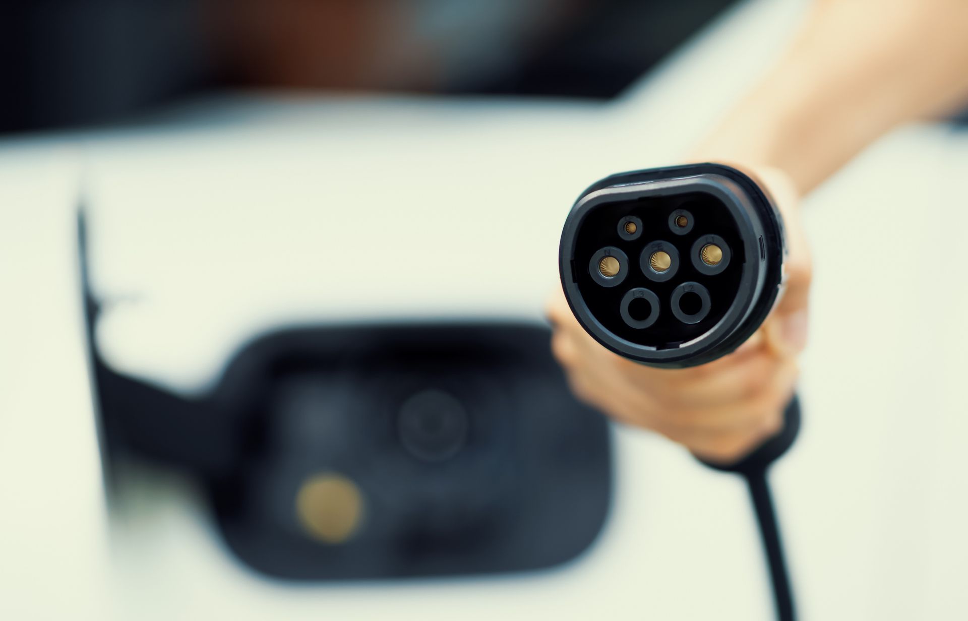 Hand holding an electric vehicle charging connector towards the car's charging port.