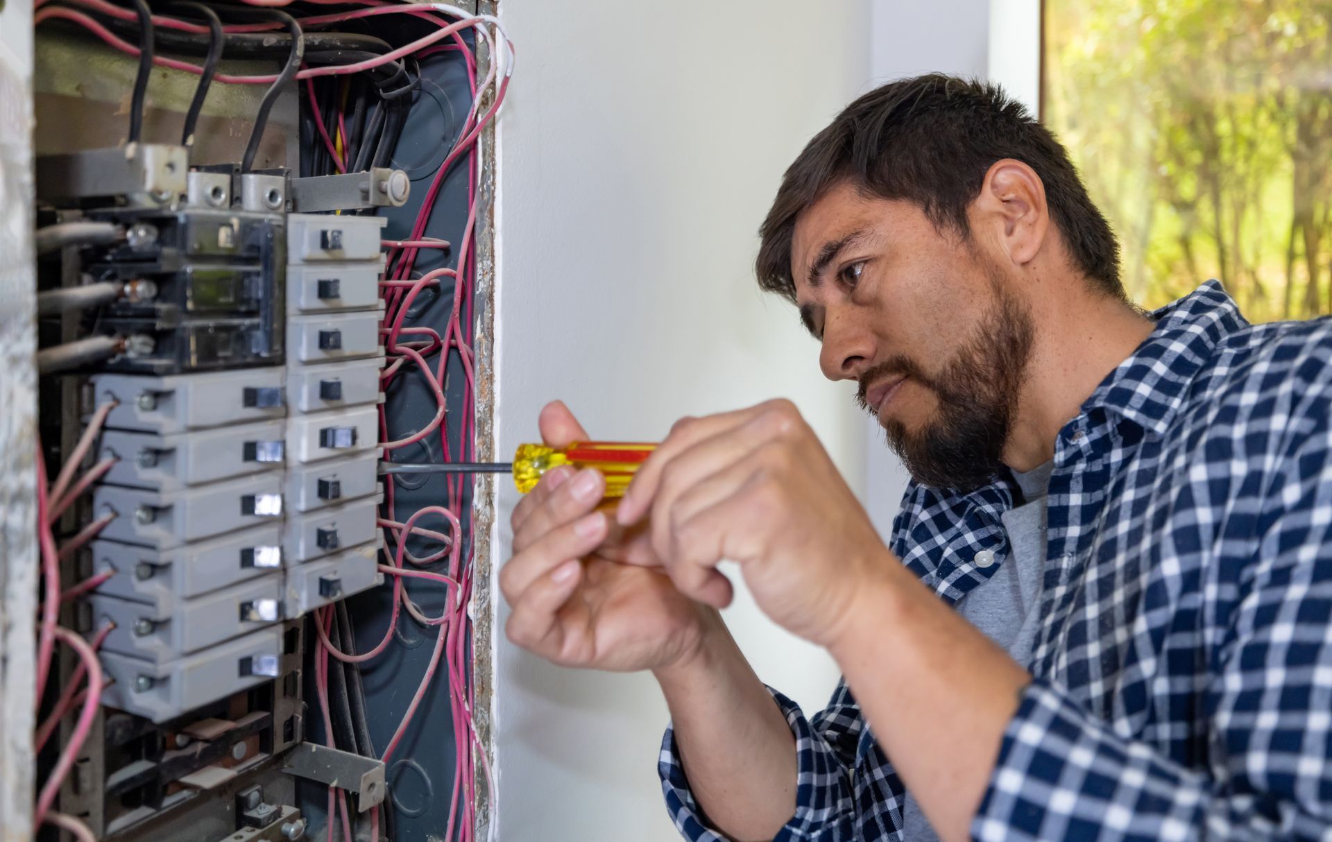Man using a screwdriver on a circuit breaker box, indoors.