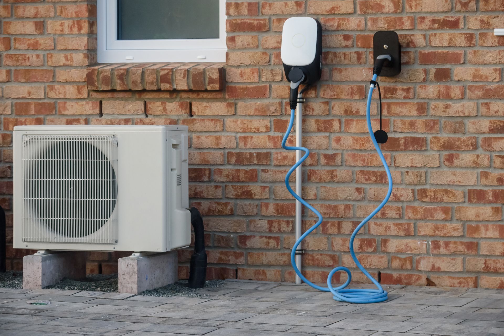 Two EV chargers and an AC unit mounted on brick wall.