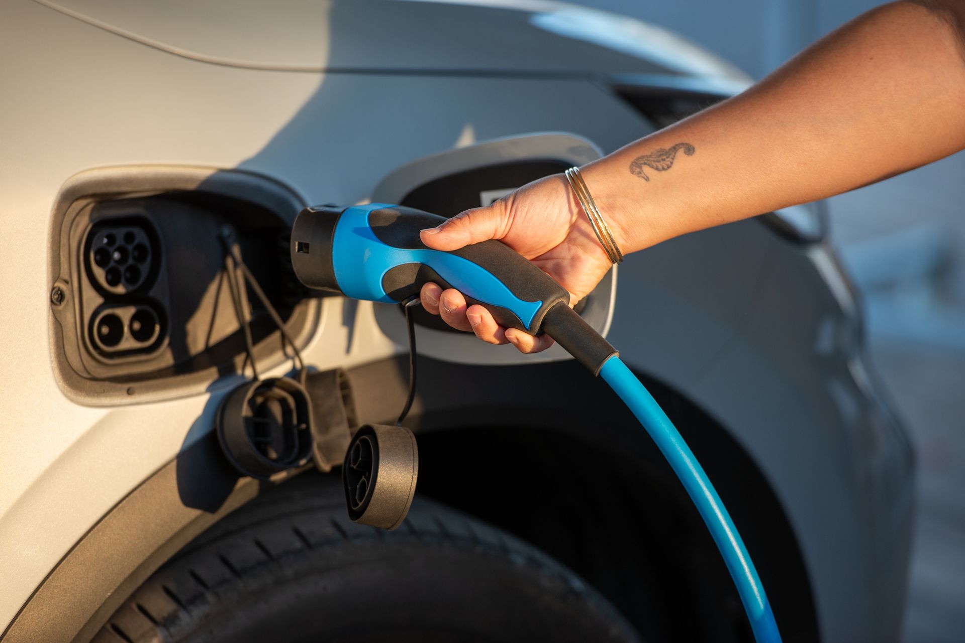 Hand plugging a blue charging cable into an electric vehicle's charging port.