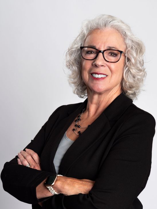 A woman is sitting at a desk with a laptop and a vase of flowers.