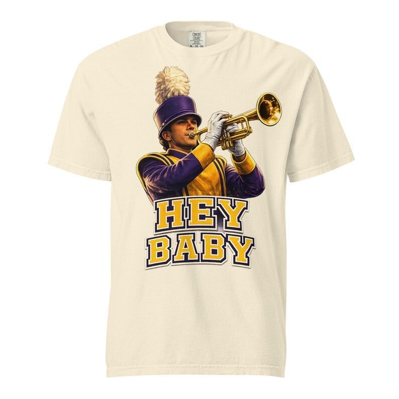 Cream-colored t-shirt featuring a marching band member in purple and gold uniform playing a trumpet above