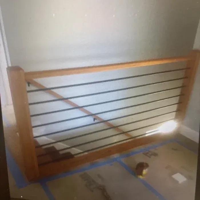 A wooden railing with horizontal metal cables installed at the top of a staircase under construction.