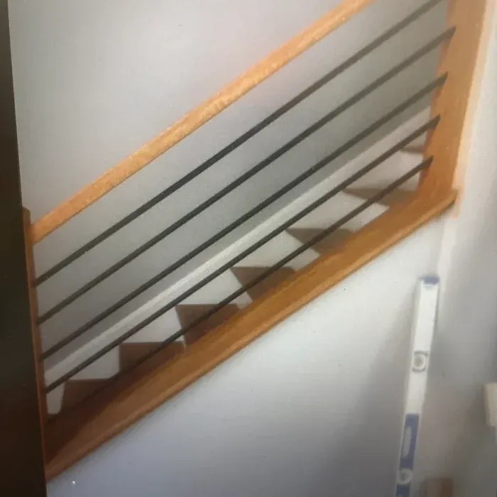 Staircase featuring light wood handrails, horizontal black metal balusters, and open wooden treads against a white wall.