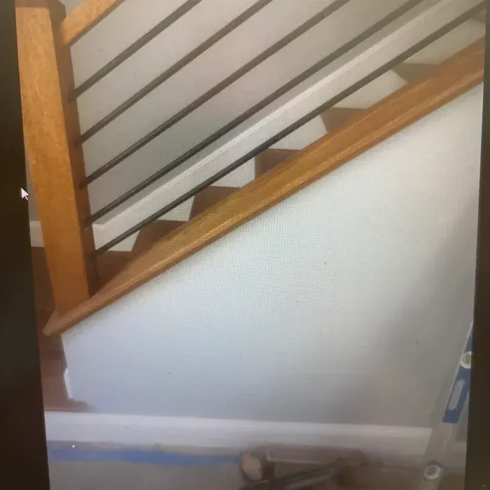 Interior staircase with a wooden handrail, vertical black metal balusters, and a white paneled wall underneath.
