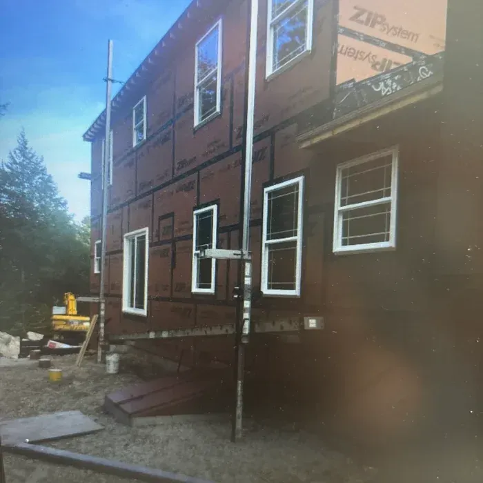 A two-story building under construction with brown ZIP System wall sheathing, white-framed windows, and exterior scaffolding.