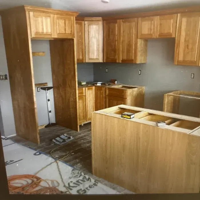 Unfinished kitchen with light wood cabinets, an island base, and a tall refrigerator enclosure under construction.