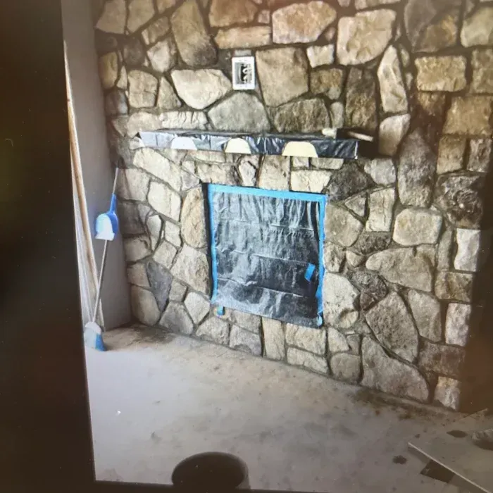 A stone-faced fireplace under construction, featuring a masked-off insert and a mantel wrapped in protective plastic.