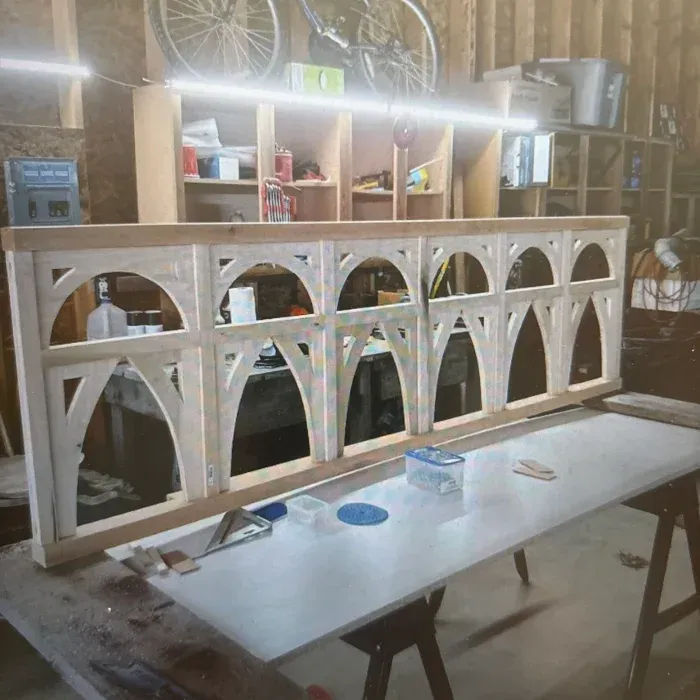 A wooden frame with five arched openings sitting on a workbench in a woodworking shop.