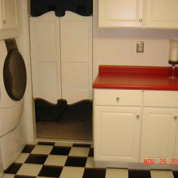 A laundry room with a white dryer, a red-countered cabinet, and saloon-style doors leading to another room.