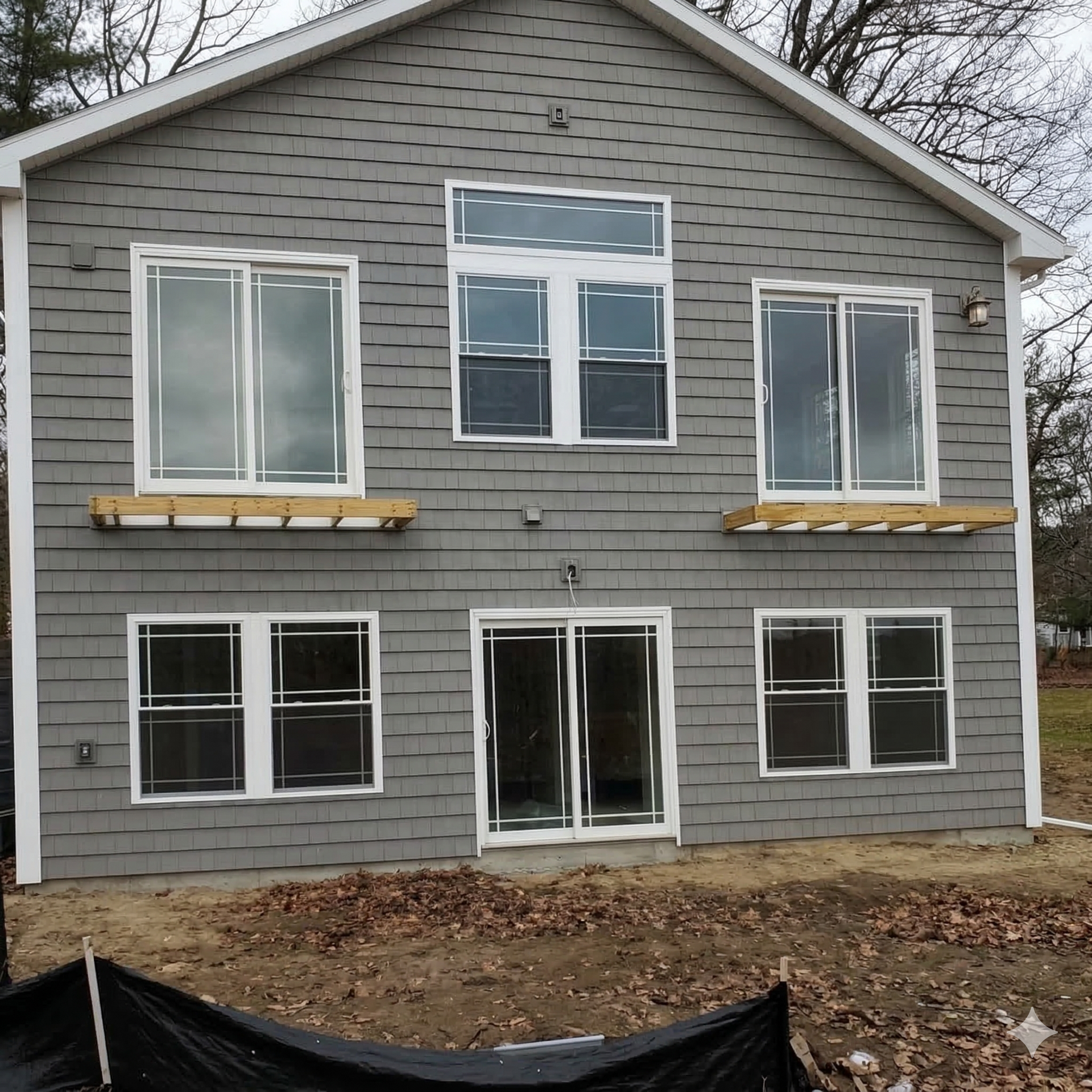 A two-story grey-sided house exterior with a sliding glass door, several windows, and unfinished wooden flower boxes.