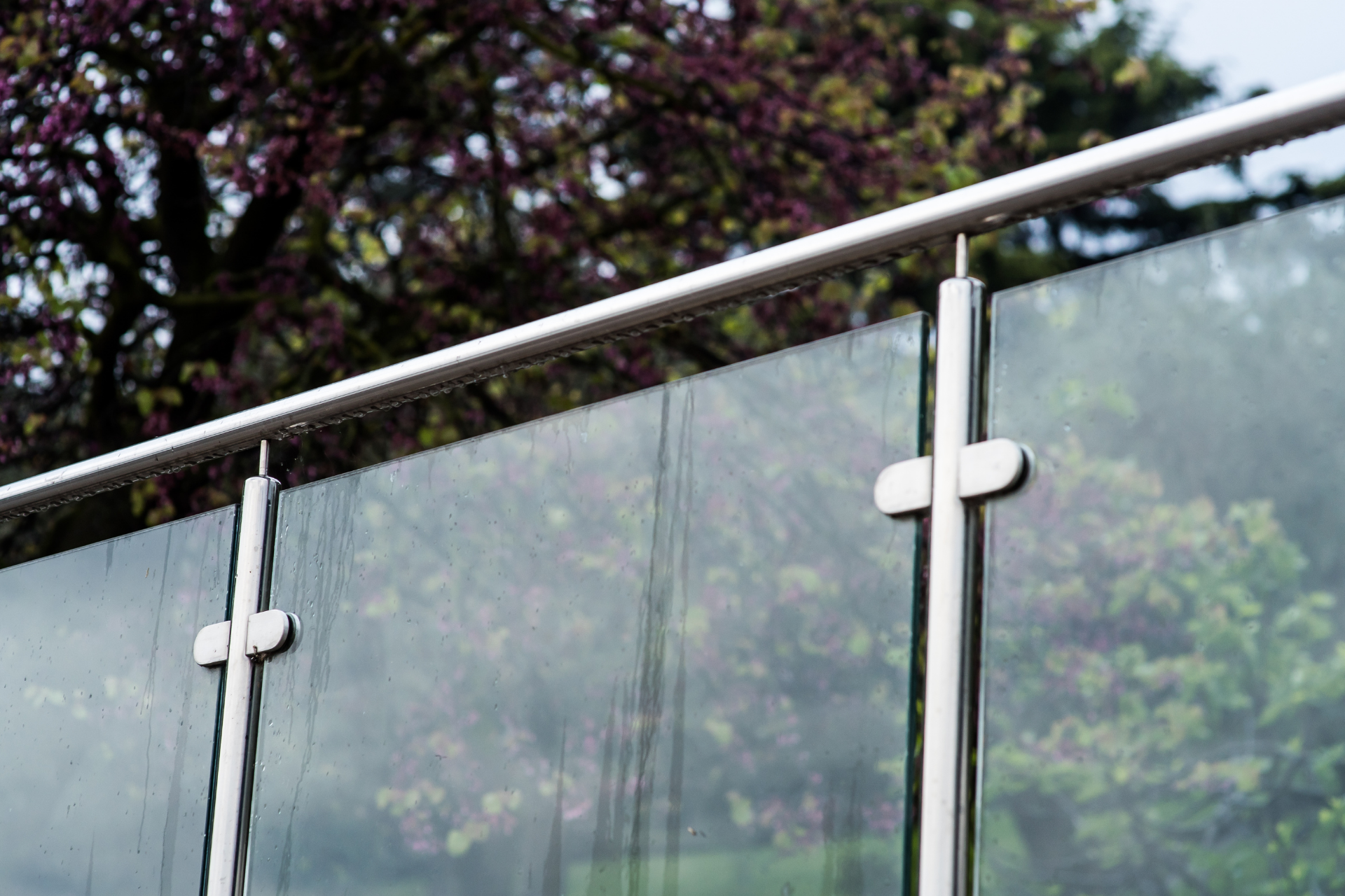 A close up of a glass railing with trees in the background.