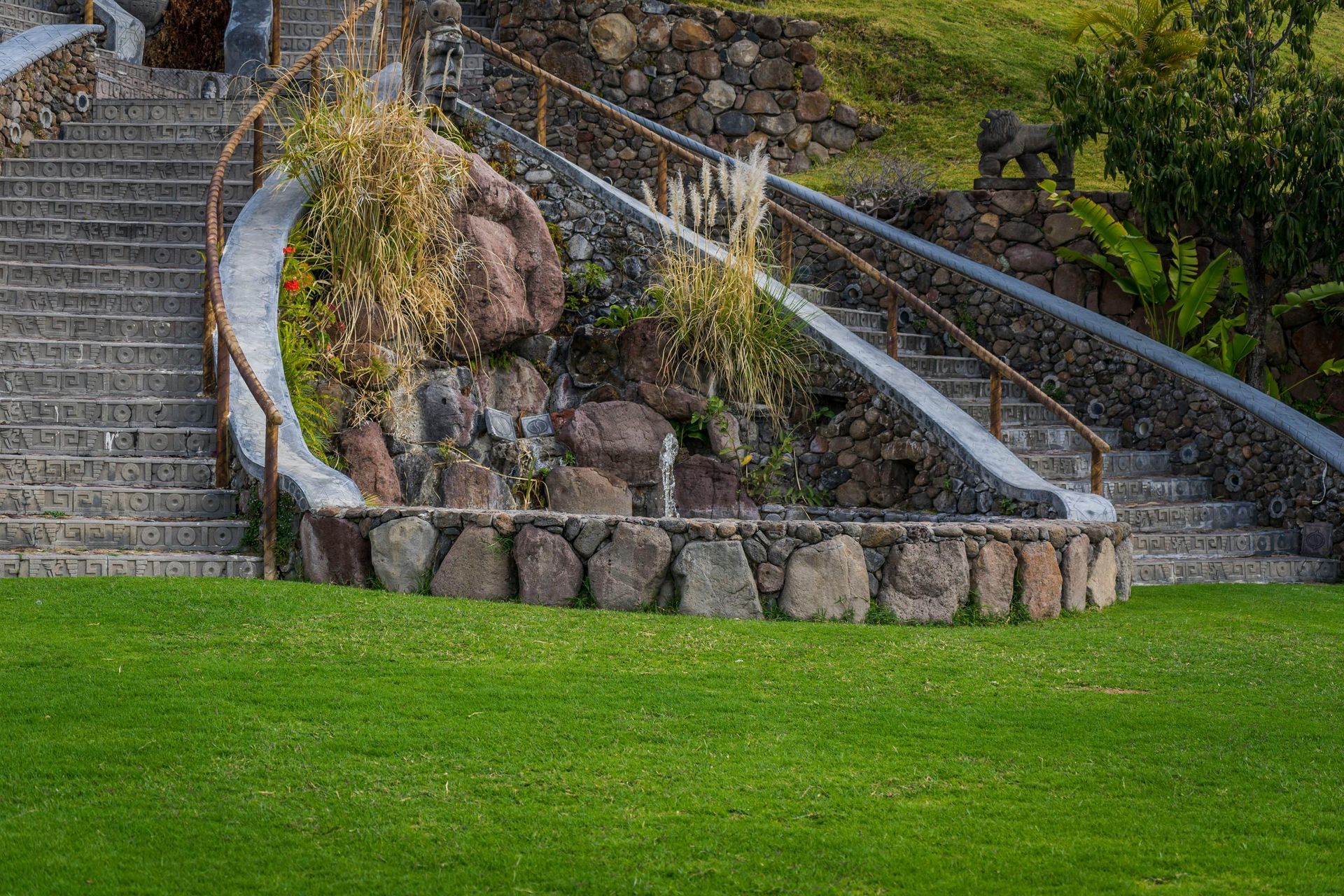 Stone stairways with metal railings beside a rocky landscaped slope and green lawn