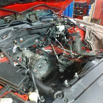 A close up of a car engine with the hood open in a garage.