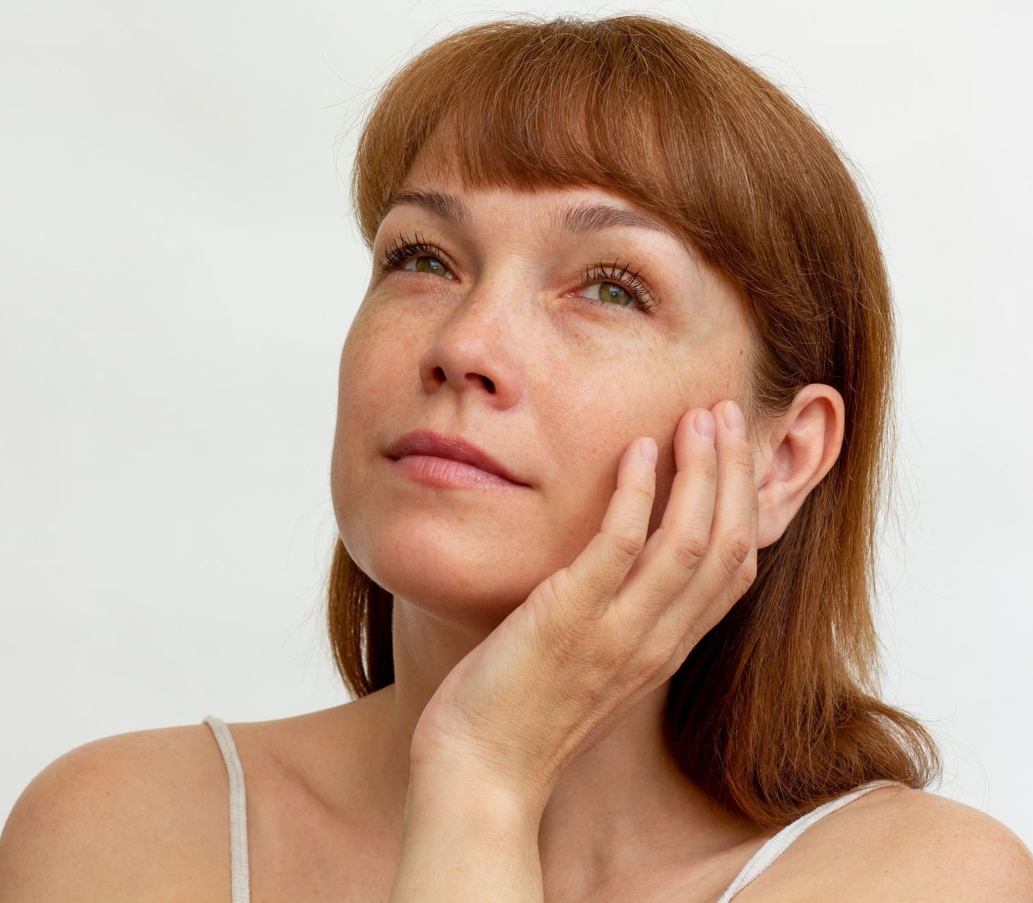 A woman is holding her hand to her face and looking up.