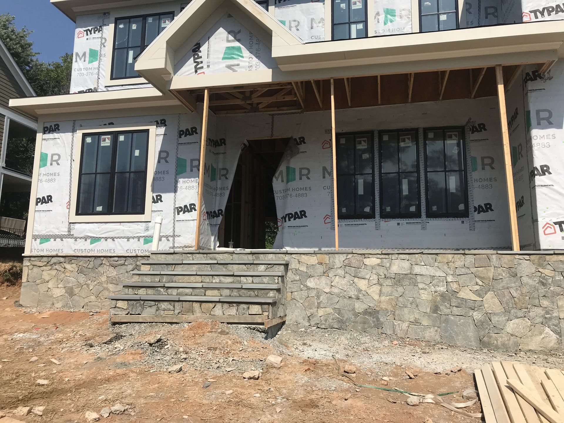 Stone-faced house under construction with dark windows, steps, and unfinished porch.