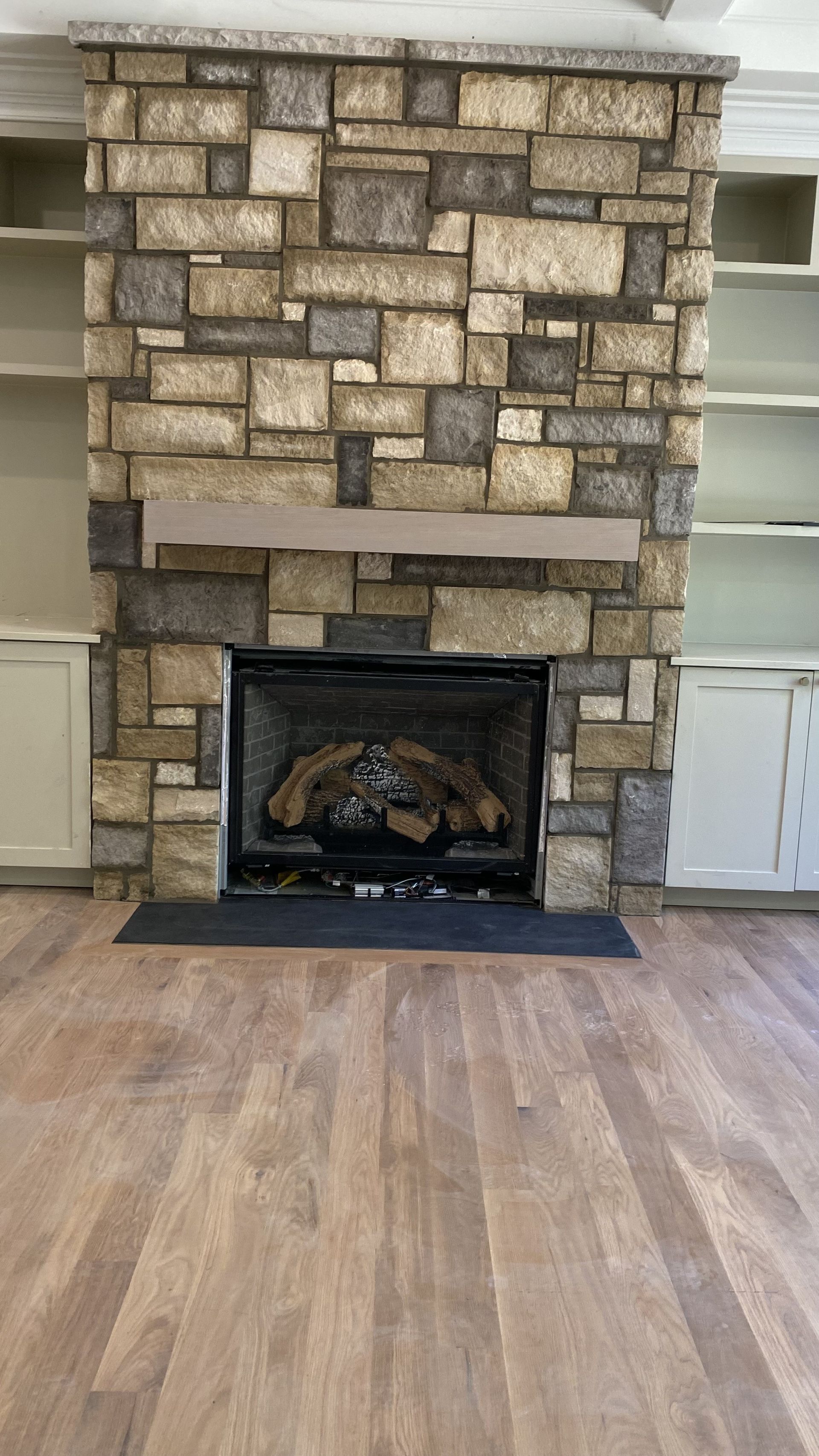 Fireplace with stone facade, wooden mantel, and built-in shelves in a room with hardwood floors.