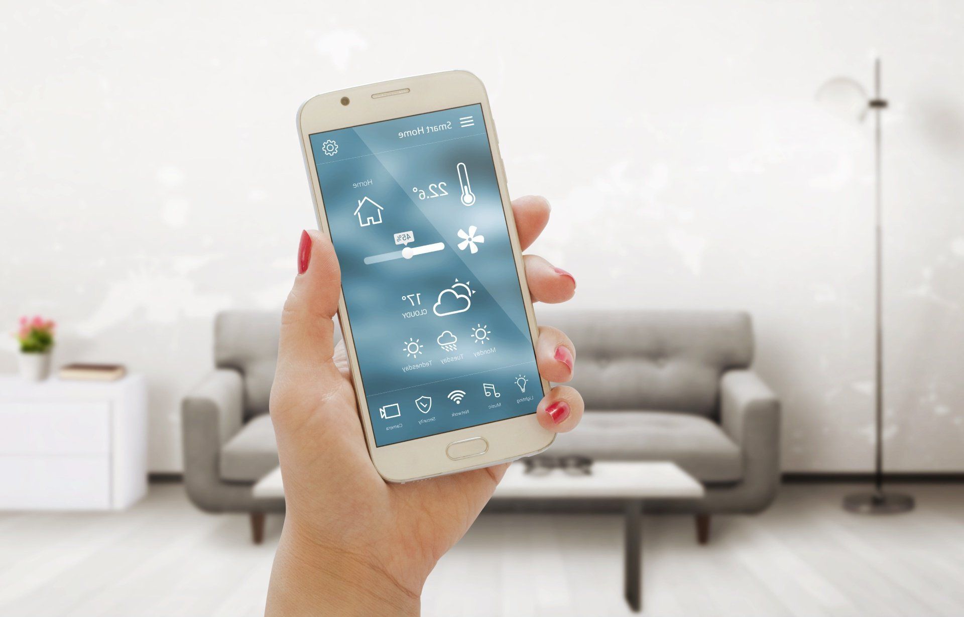 Mano di donna che tiene in mano uno smartphone su cui è visualizzata l'interfaccia di un'app per la casa intelligente in un soggiorno.