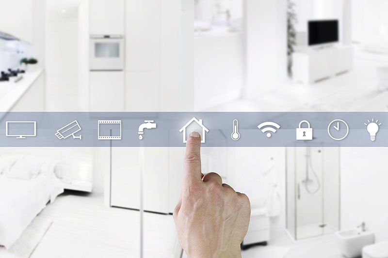 Mano che indica l'icona di una casa sul pannello di controllo di una casa intelligente, con uno sfondo interno bianco.