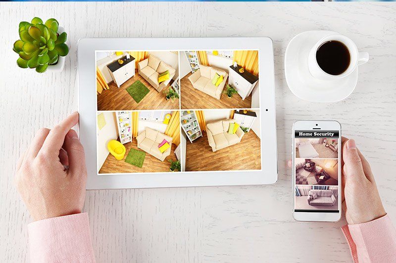 Persona che guarda il filmato della telecamera di sicurezza domestica su un tablet e un telefono, vista dall'alto.