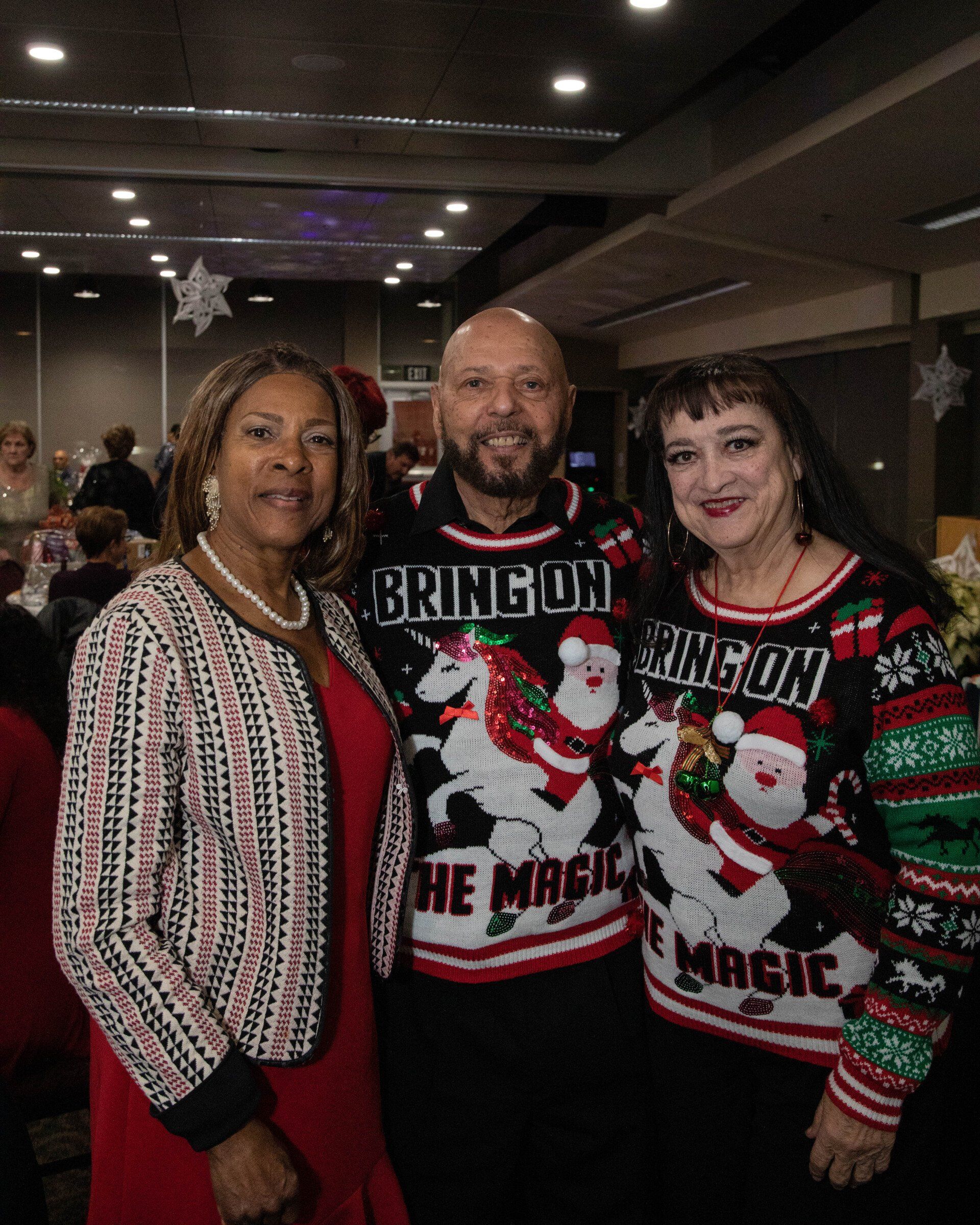 Three people pose indoors, two wearing