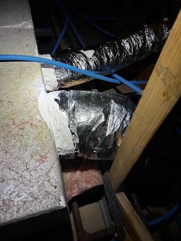 A picture of a duct in an attic with a light on it.