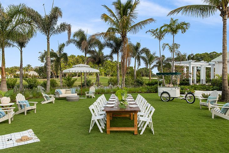 A long table and chairs are sitting on a lush green field.