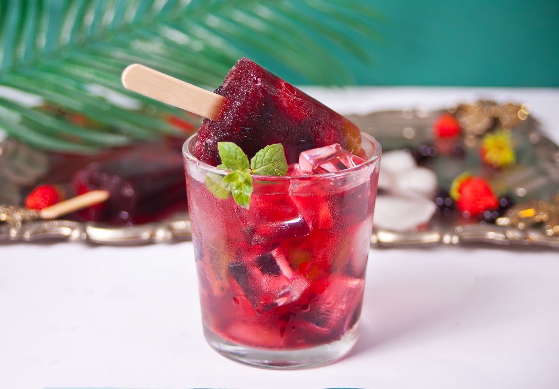 A glass of red liquid with a popsicle on a stick in it.