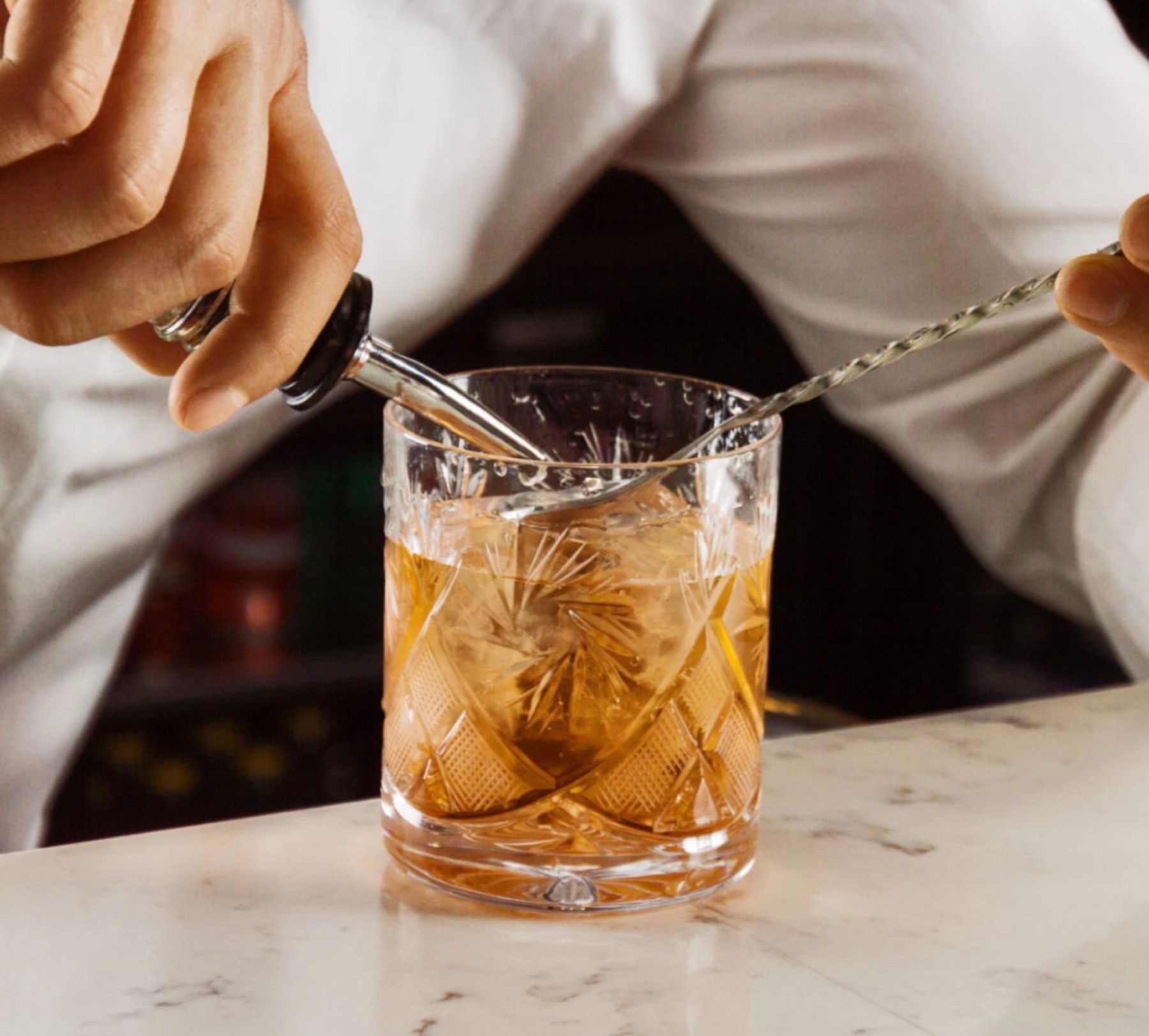 A person is stirring a drink in a glass with a spoon
