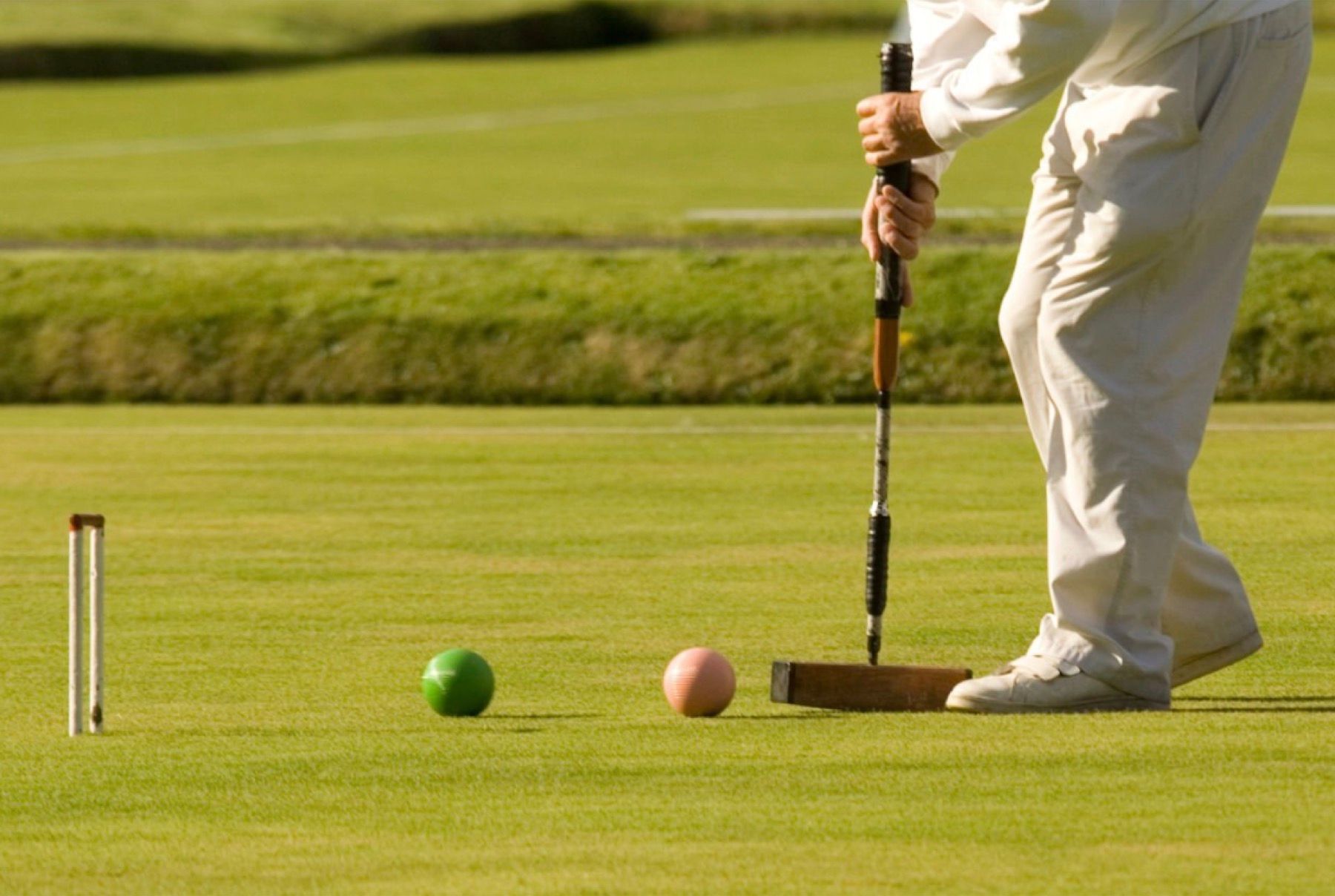 A person is playing a game of croquet on a lush green field
