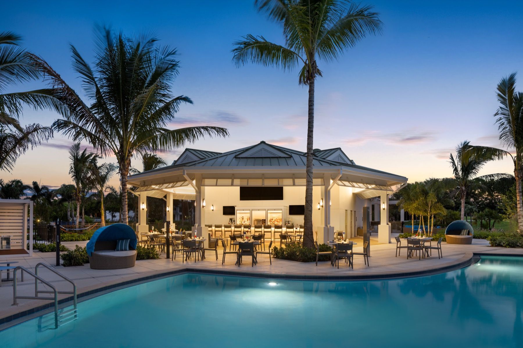 A large swimming pool with a bar in the middle of it surrounded by palm trees.